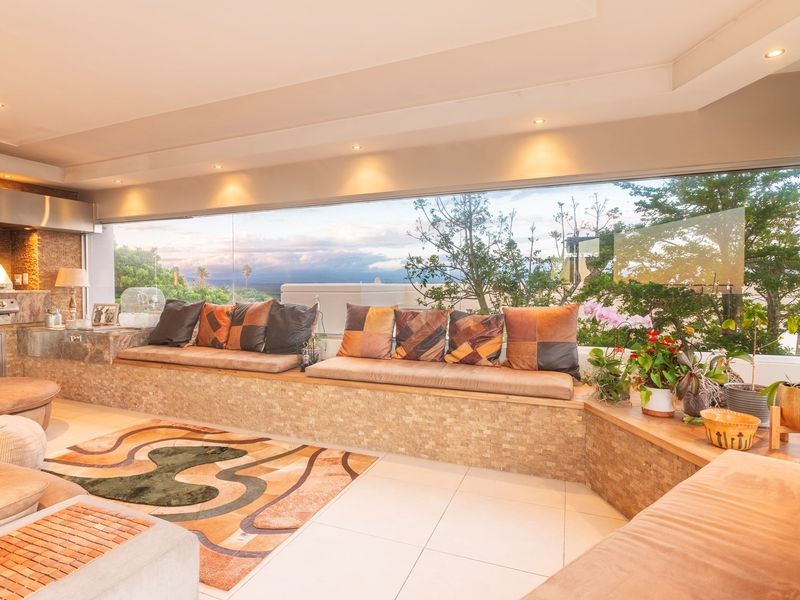 A spacious covered patio featuring built-in stone bench seating, an integrated outdoor grill, and expansive windows offering scenic views.