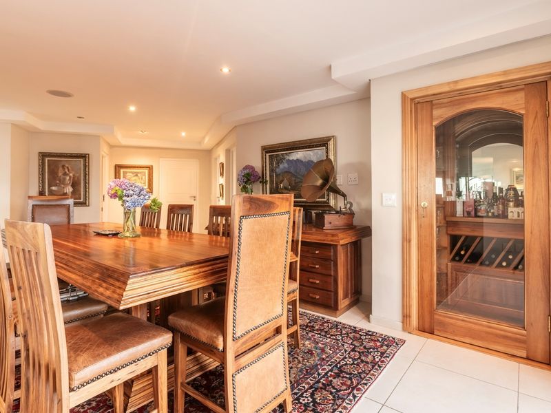A well-appointed dining room featuring tiled flooring, recessed lighting, and a custom-built timber wine cellar with a glass door.