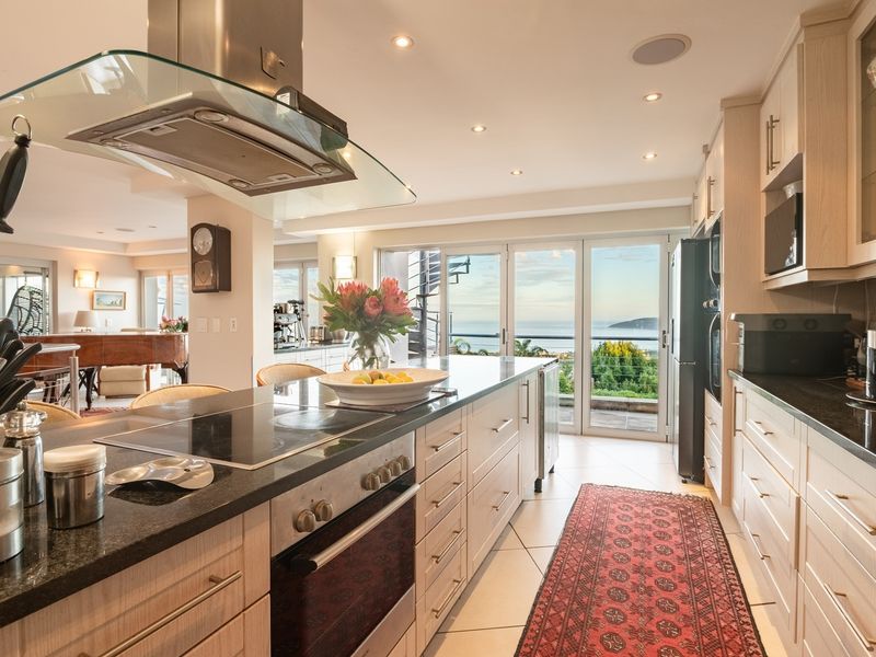 Spacious open-plan kitchen featuring modern cabinetry, stone countertops, and integrated appliances, flowing seamlessly toward a balcony with scenic coastal views.