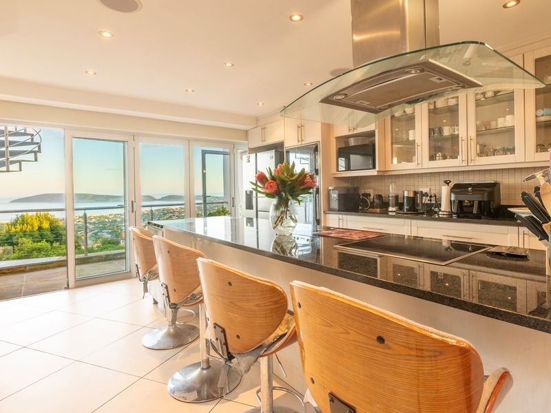 Modern kitchen featuring granite countertops, built-in cabinetry, and a glass extractor hood, with seamless access to a balcony offering expansive coastal views.