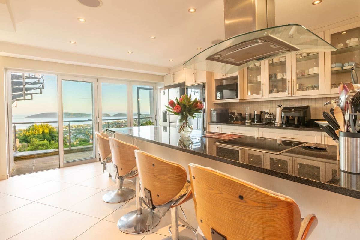 Modern kitchen featuring granite countertops, built-in cabinetry, and a glass extractor hood, with seamless access to a balcony offering expansive coastal views.