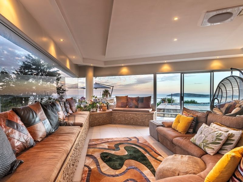 Spacious living area featuring extensive built-in seating, floor-to-ceiling glass walls, and seamless access to an outdoor patio with panoramic ocean views.