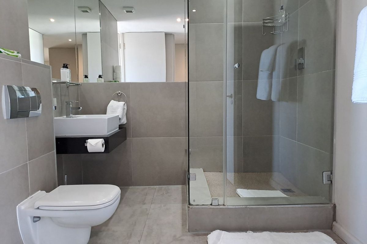 Modern bathroom featuring a wall-mounted toilet, floating vanity with vessel sink, and a spacious glass-enclosed shower with neutral grey tiling.