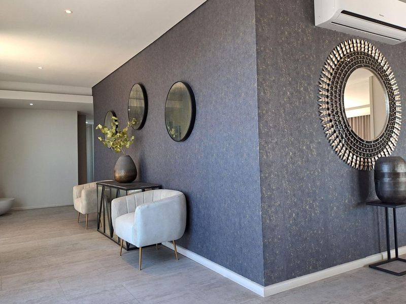 A modern living area featuring textured feature walls, tiled flooring, recessed lighting, and a wall-mounted split-system air conditioning unit.