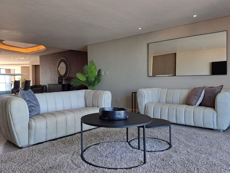 A well-maintained living room featuring recessed downlighting and a large wall-mounted mirror, creating a bright and spacious atmosphere.