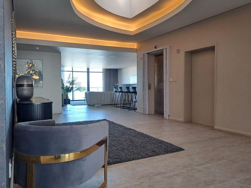 Spacious open-plan living area featuring a private elevator entrance, modern recessed ceiling lighting, and large glass doors leading to an outdoor space.