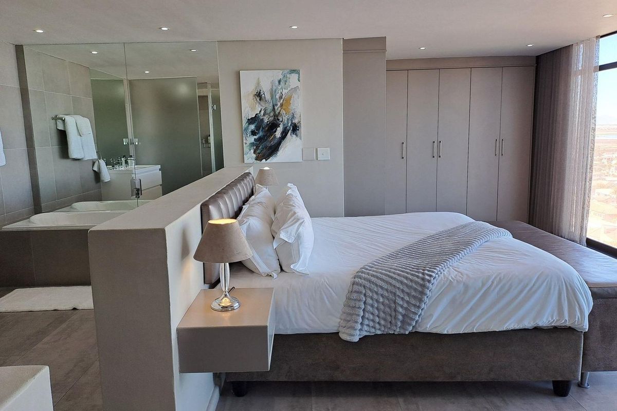 Modern bedroom featuring built-in cupboards, recessed lighting, and an open-plan en-suite bathroom with a bathtub and vanity.