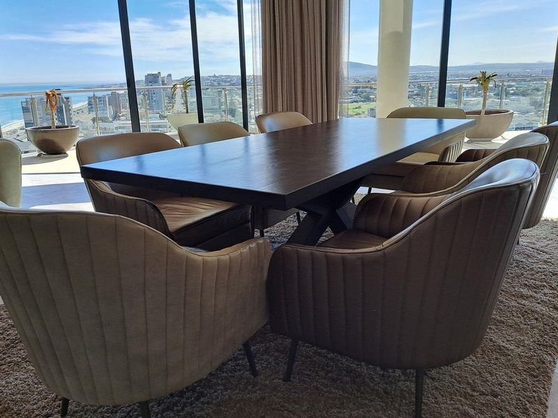 Elegant dining area featuring floor-to-ceiling windows with expansive coastal and city views, seamlessly connecting to an outdoor balcony space.
