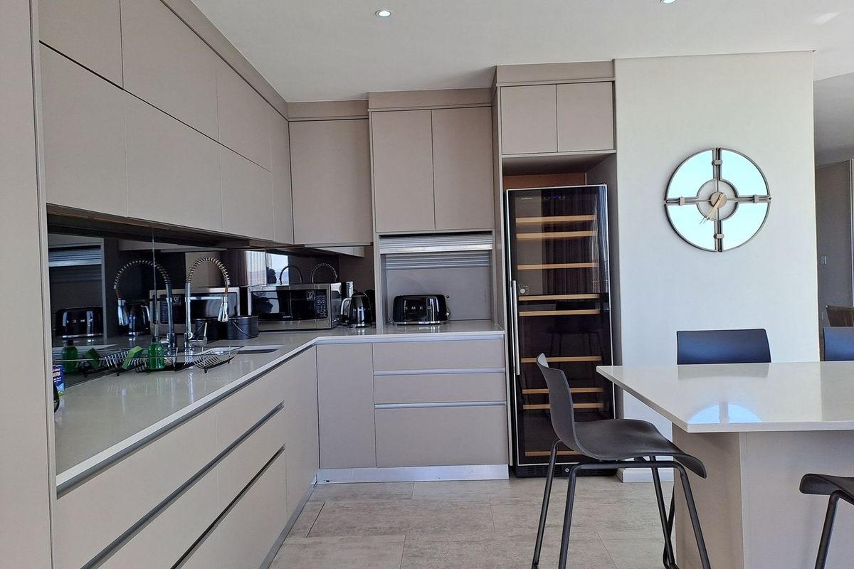 Modern kitchen featuring sleek handleless cabinetry, stone countertops, a mirrored splashback, and an integrated wine cooler, creating a sophisticated and functional culinary space.
