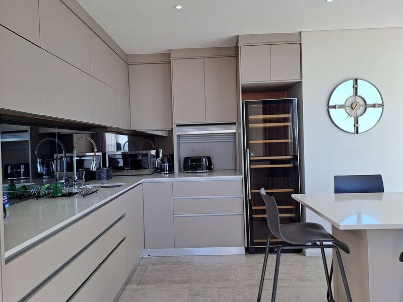Modern kitchen featuring sleek handleless cabinetry, stone countertops, a mirrored splashback, and an integrated wine cooler, creating a sophisticated and functional culinary space.