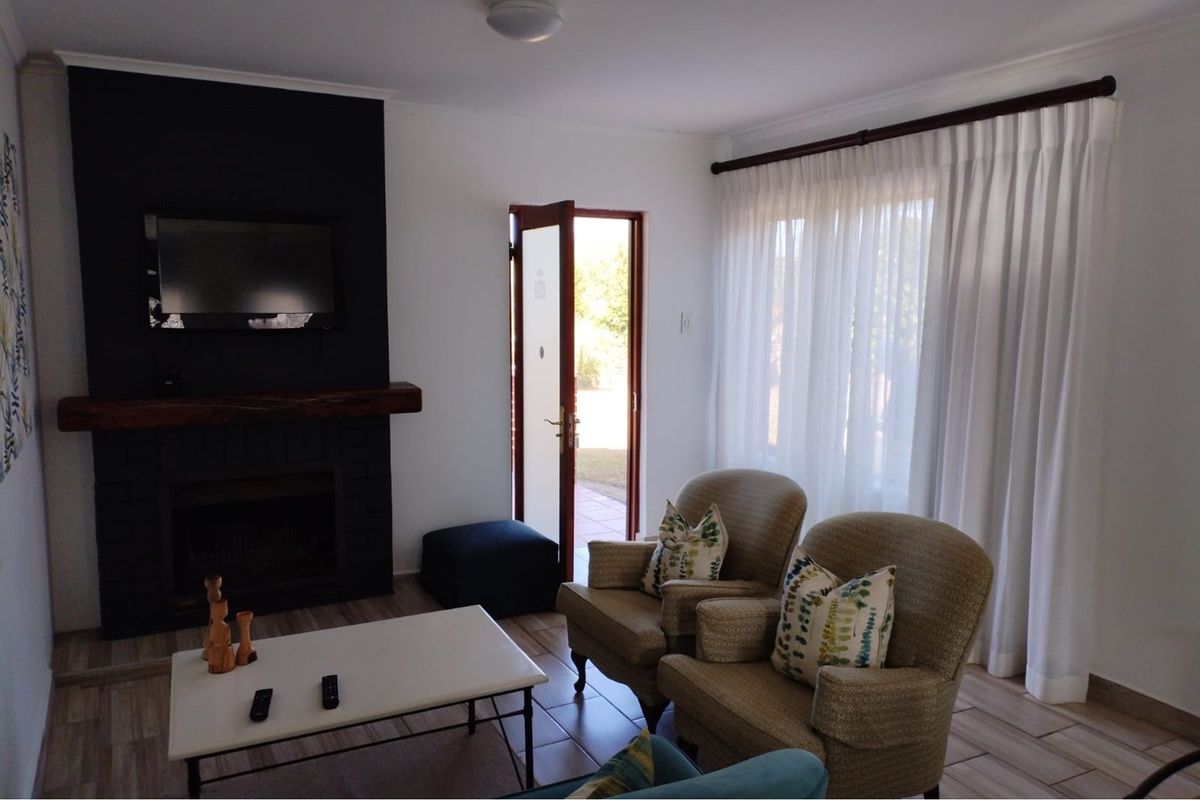 A cozy living room featuring a dark-painted fireplace with a wooden mantel, tiled flooring, and direct access to an outdoor area through a glass door.