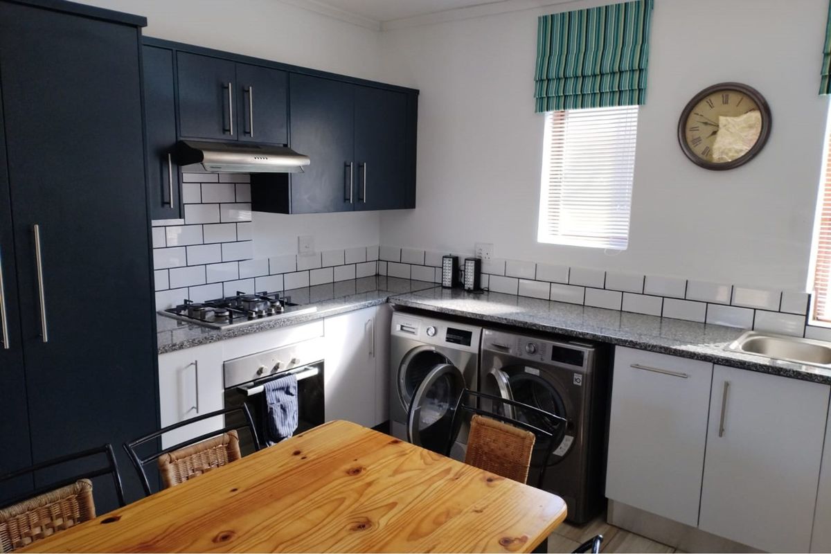 Modern kitchen featuring dark upper cabinetry, white lower cabinets, granite countertops, subway tile backsplash, built-in oven, gas hob, and integrated laundry appliances.