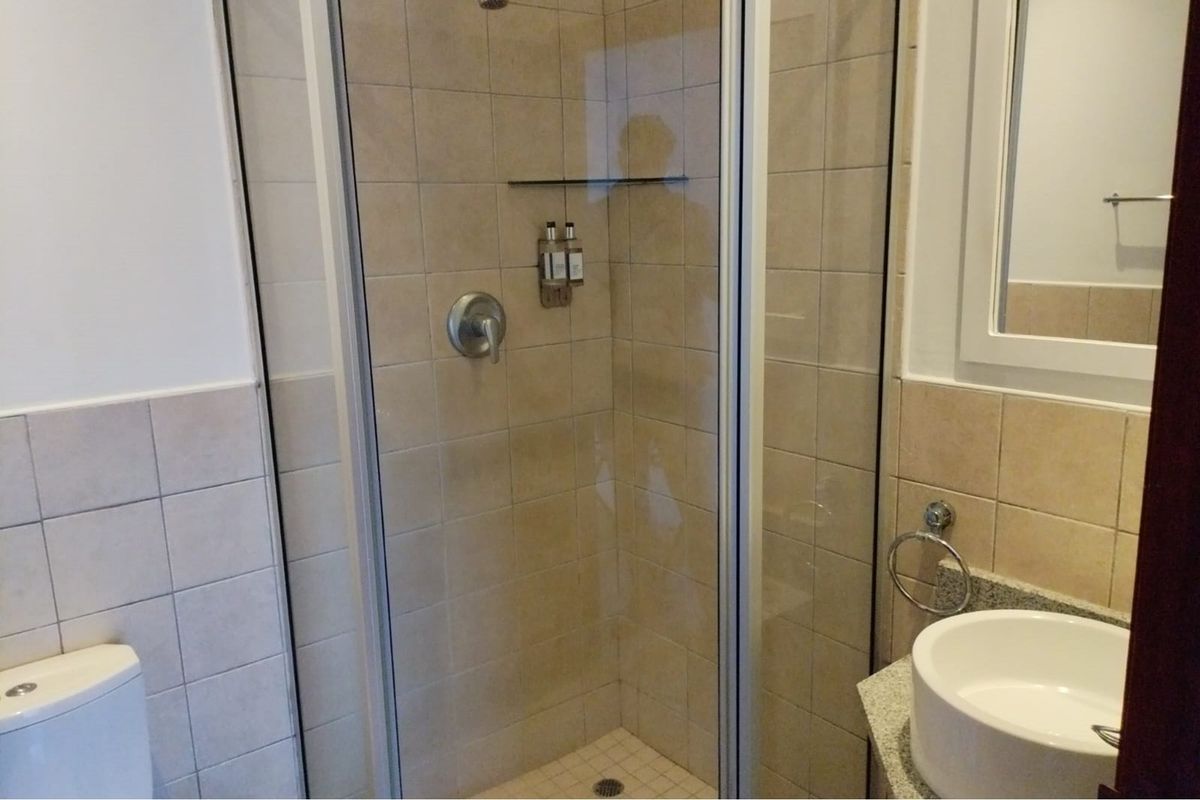 A functional bathroom featuring a glass-enclosed shower, tiled walls, a modern vessel sink, and a standard toilet.