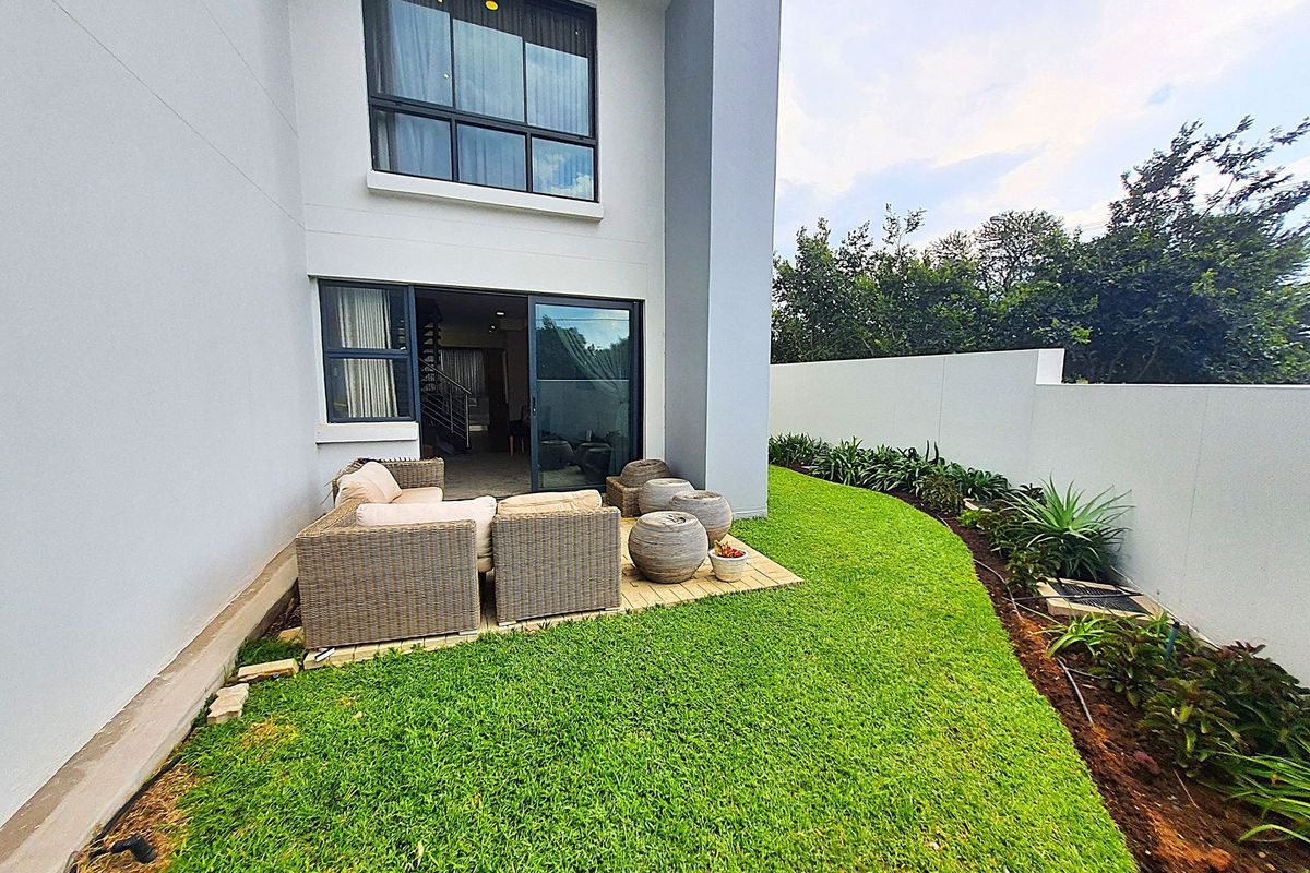 A private rear garden featuring a paved patio area, manicured lawn, and perimeter boundary wall, accessible via sliding glass doors from the interior.