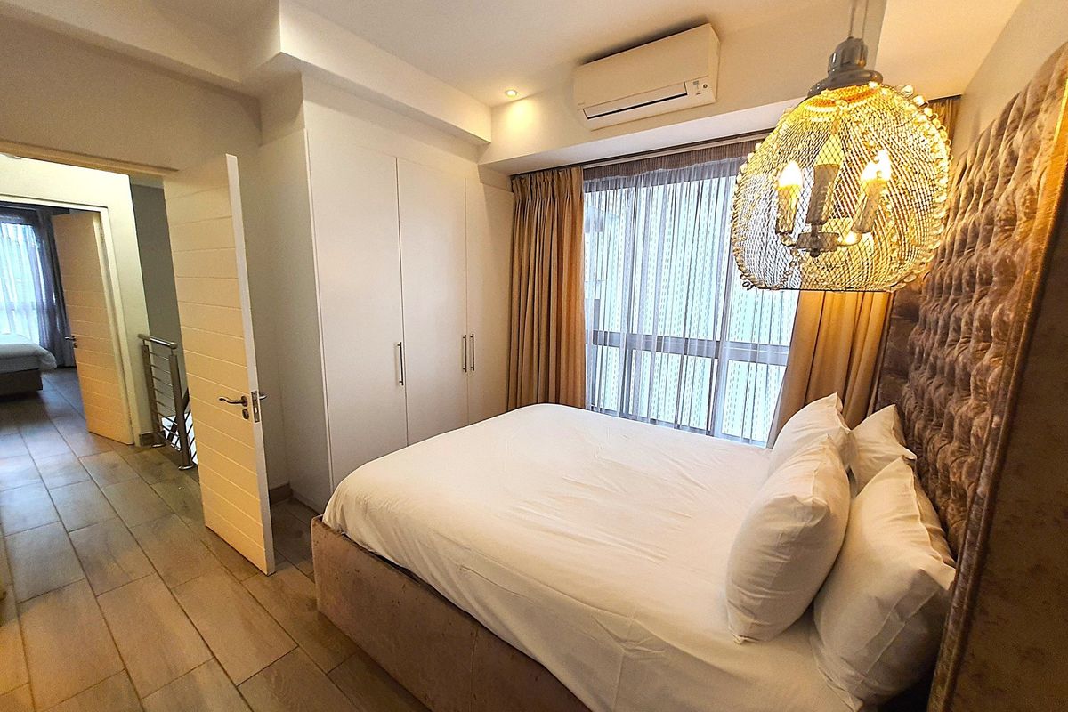 A well-appointed bedroom featuring built-in wardrobes, a wall-mounted air conditioning unit, and large windows with sheer curtains, providing a bright and comfortable living space.