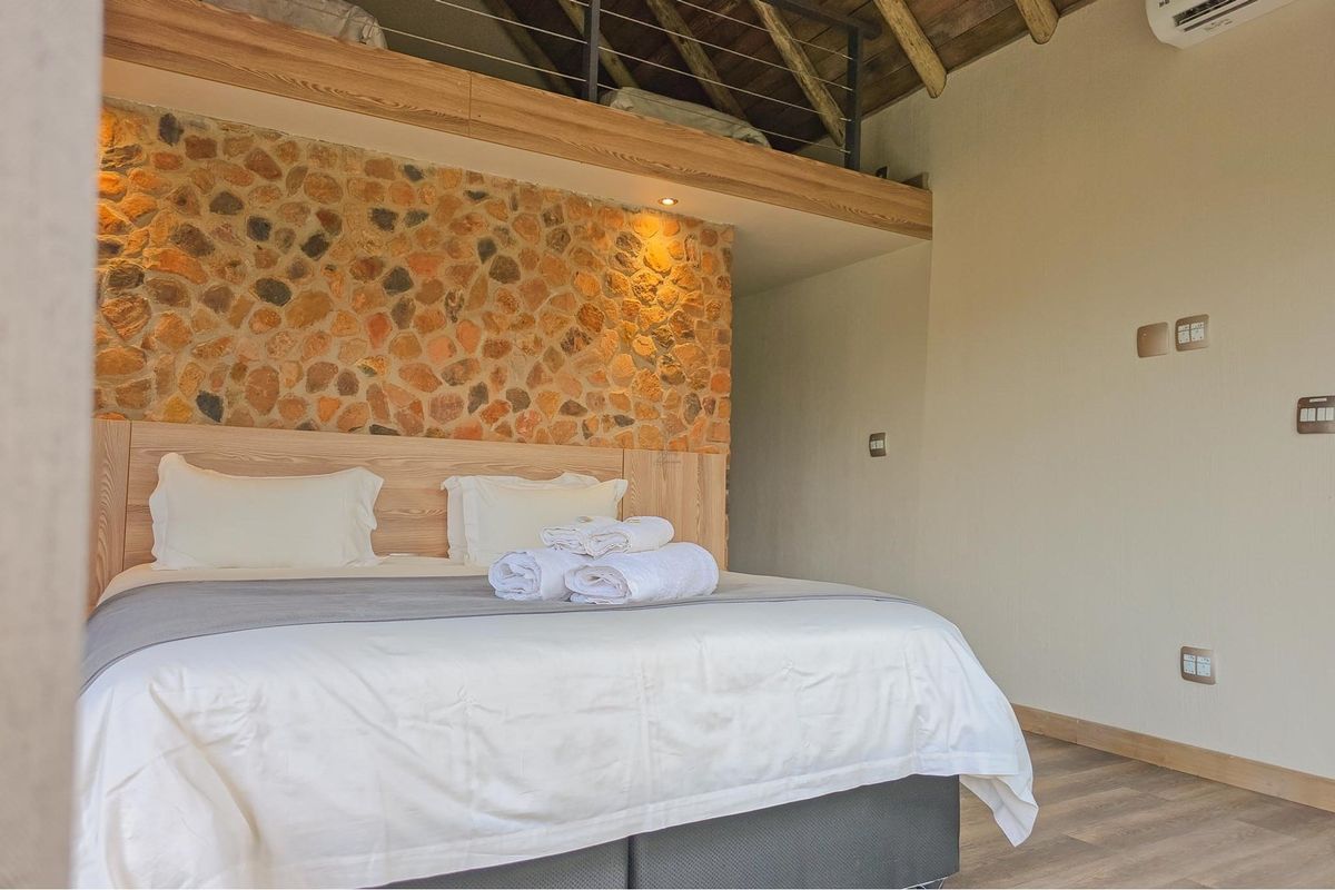 A well-maintained bedroom featuring a rustic stone accent wall, exposed timber rafters, and a mezzanine loft level, creating a warm and inviting atmosphere.