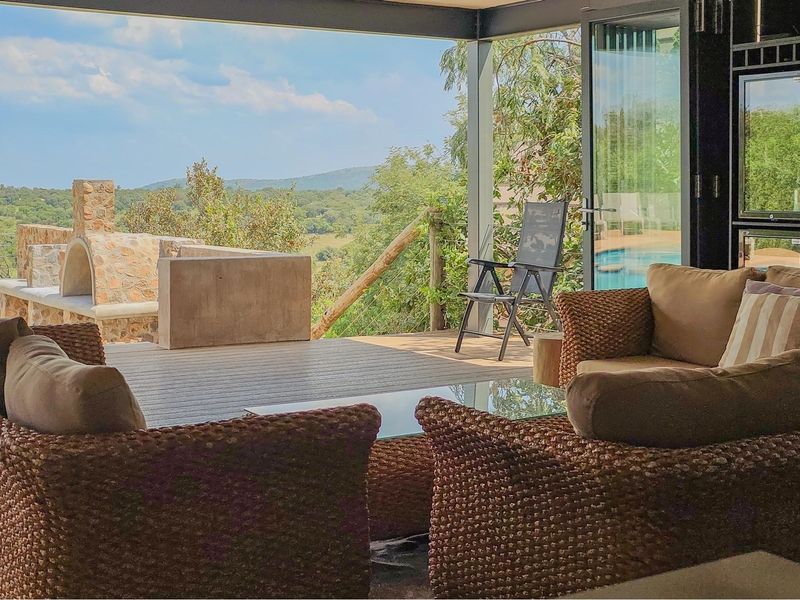 Covered outdoor patio featuring a stone pizza oven, timber decking, and bi-fold doors opening to scenic landscape views.