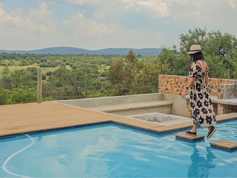 Outdoor pool area featuring timber decking, a stone-clad fire pit, built-in concrete seating, and expansive views of the surrounding landscape.