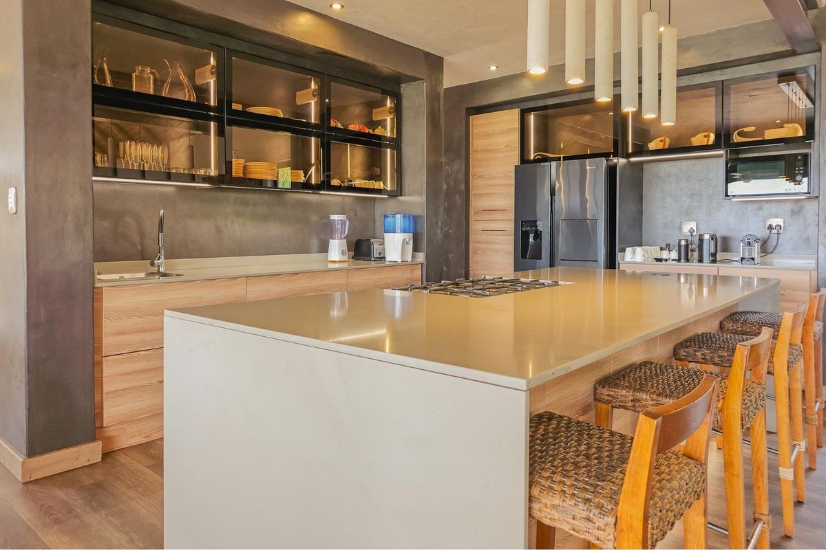 Modern kitchen featuring a large central island with stone countertops, integrated gas hob, sleek wood cabinetry, and stylish glass-front display units.