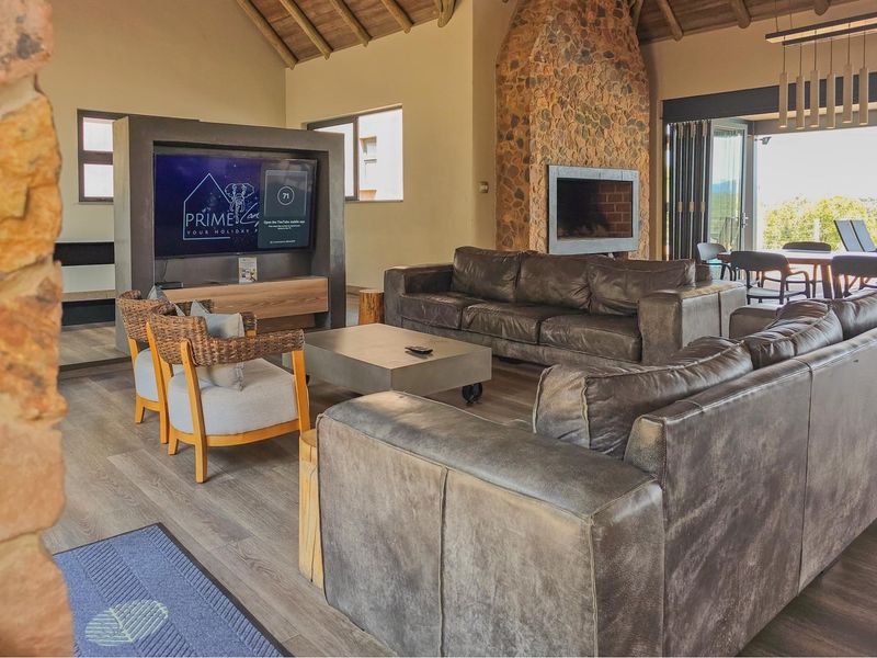 Spacious open-plan living area featuring a striking stone fireplace, vaulted timber ceilings, and seamless flow to the outdoor patio through stacking glass doors.
