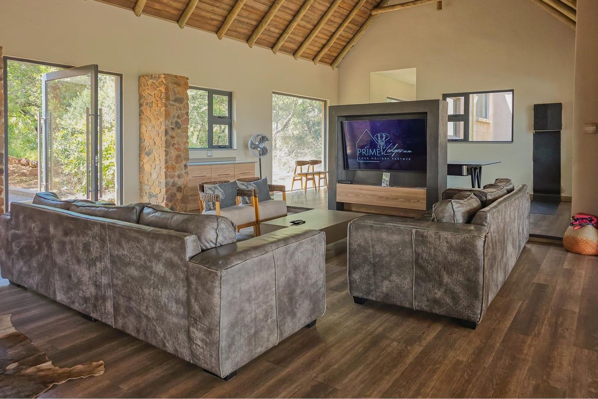 Spacious living room featuring a high vaulted ceiling with exposed timber rafters, stone accent detailing, and modern laminate flooring with large windows.