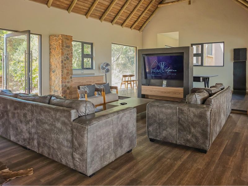 Spacious living room featuring a high vaulted ceiling with exposed timber rafters, stone accent detailing, and modern laminate flooring with large windows.