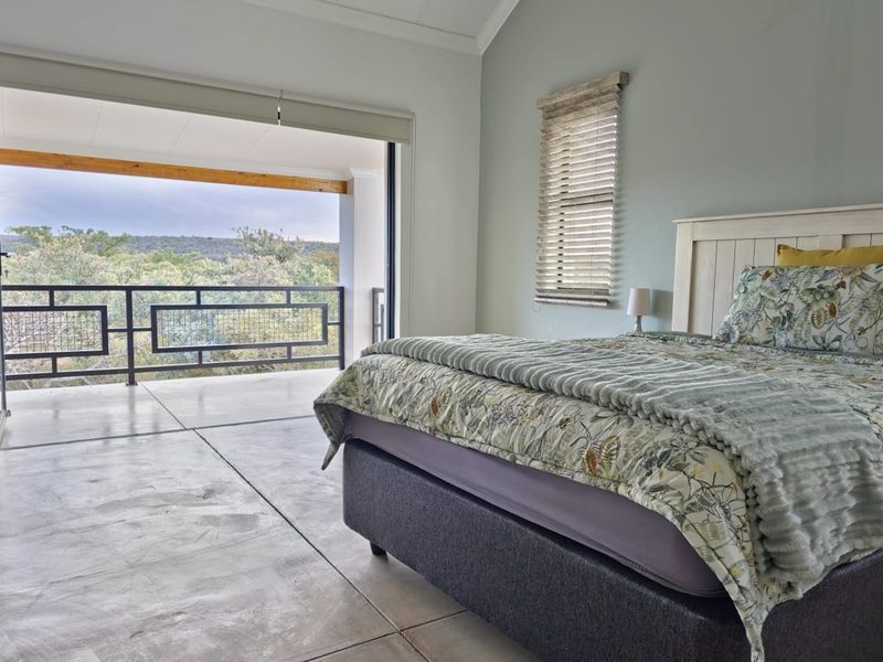 Spacious bedroom featuring polished concrete flooring, high ceilings, and large sliding doors opening onto a private balcony with scenic nature views.