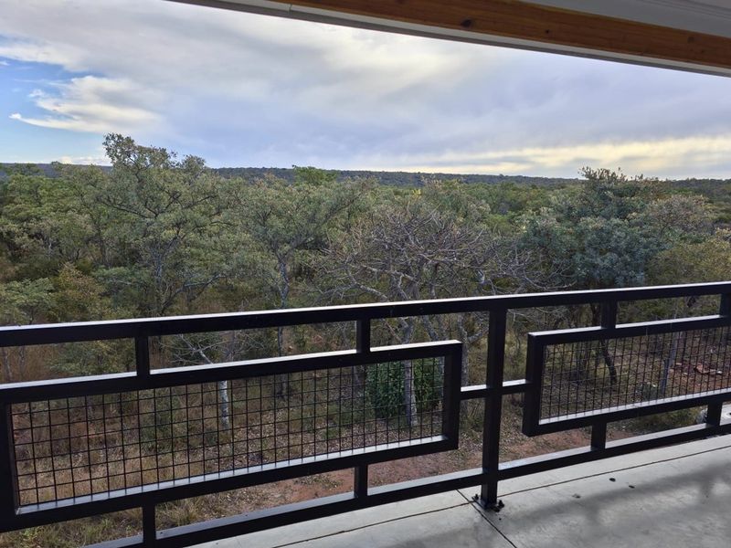 A covered balcony featuring a modern black metal railing with wire mesh infill, offering expansive views of the surrounding natural bushveld landscape.