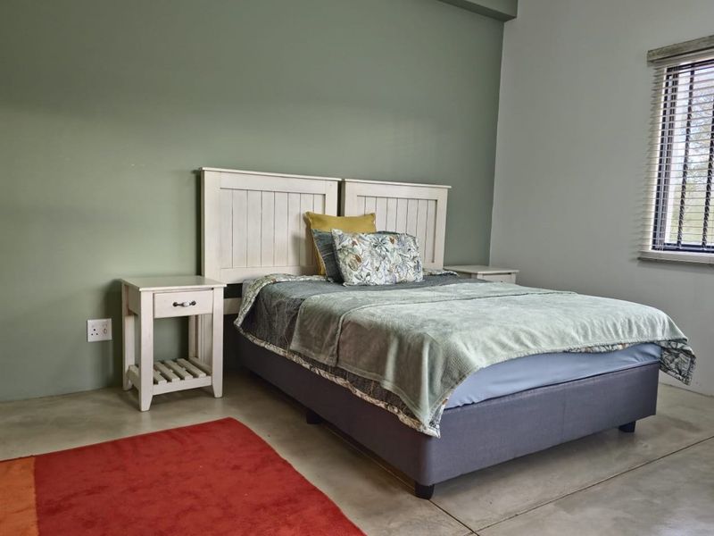 A well-maintained bedroom featuring polished concrete flooring, a sage green accent wall, and a window fitted with horizontal blinds.