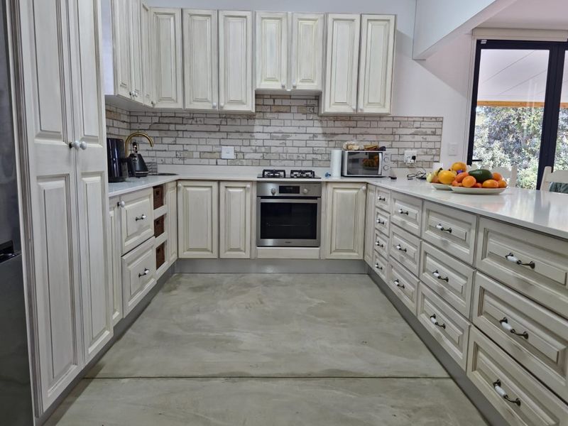 A well-appointed kitchen featuring light-toned cabinetry, a built-in oven, gas hob, and a brick-style backsplash, complemented by a polished concrete floor.