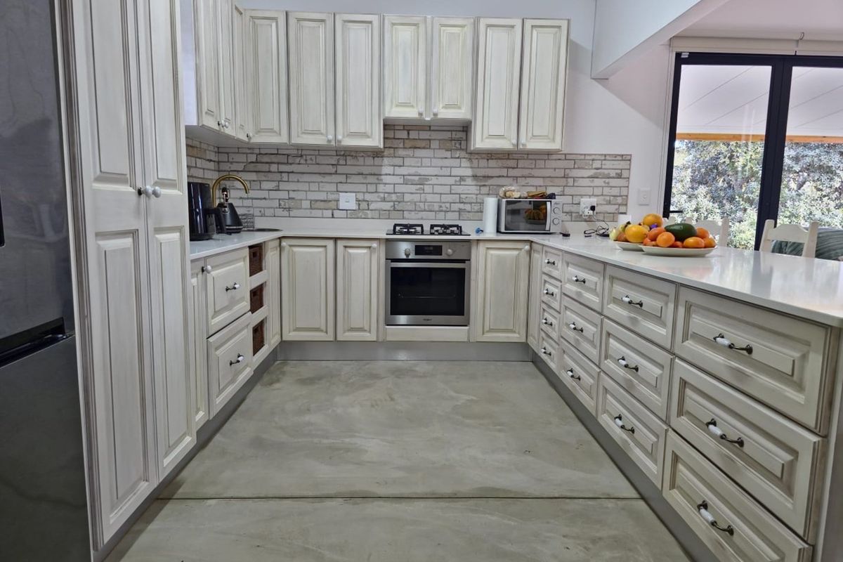 A well-appointed kitchen featuring light-toned cabinetry, a built-in oven, gas hob, and a brick-style backsplash, complemented by a polished concrete floor.