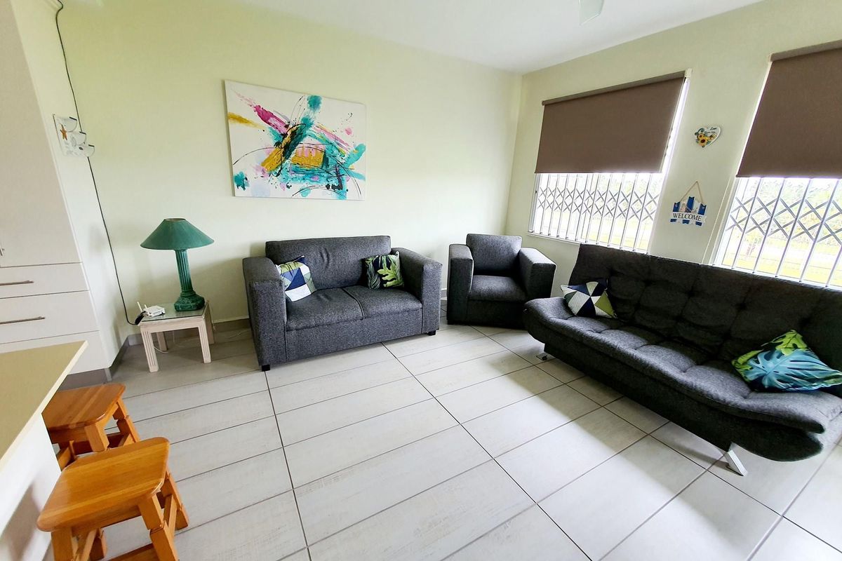 A bright living area featuring neutral tiled flooring, large windows with fitted roller blinds, and security gates for added peace of mind.