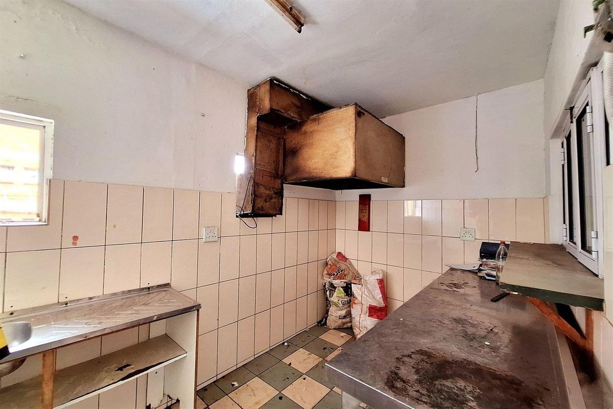 A commercial kitchen space featuring tiled walls, stainless steel work surfaces, and a large extractor hood, requiring significant refurbishment and cleaning.