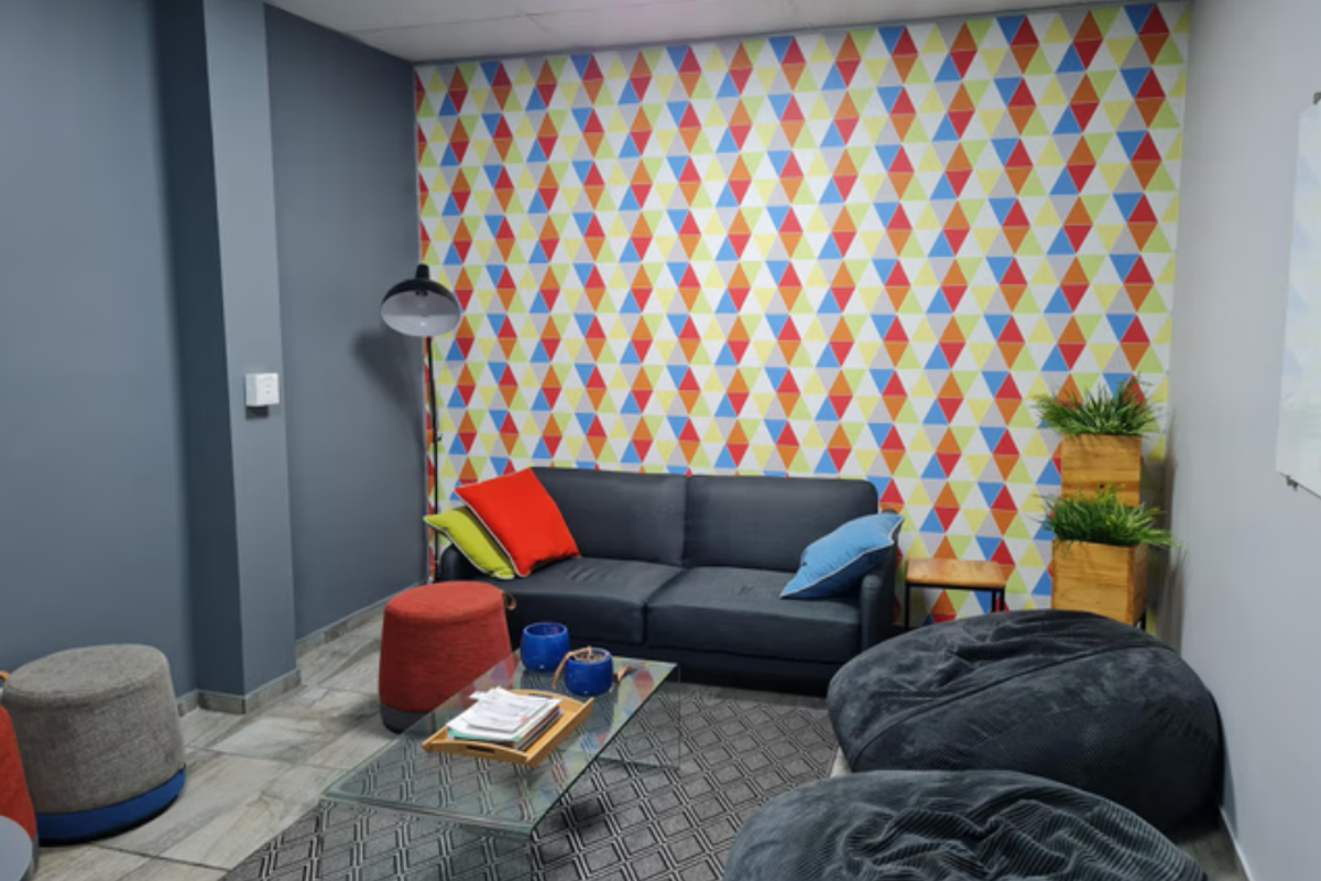 A casual breakout or lounge area featuring a vibrant geometric patterned accent wall and tiled flooring, suitable for office or industrial workspace relaxation.