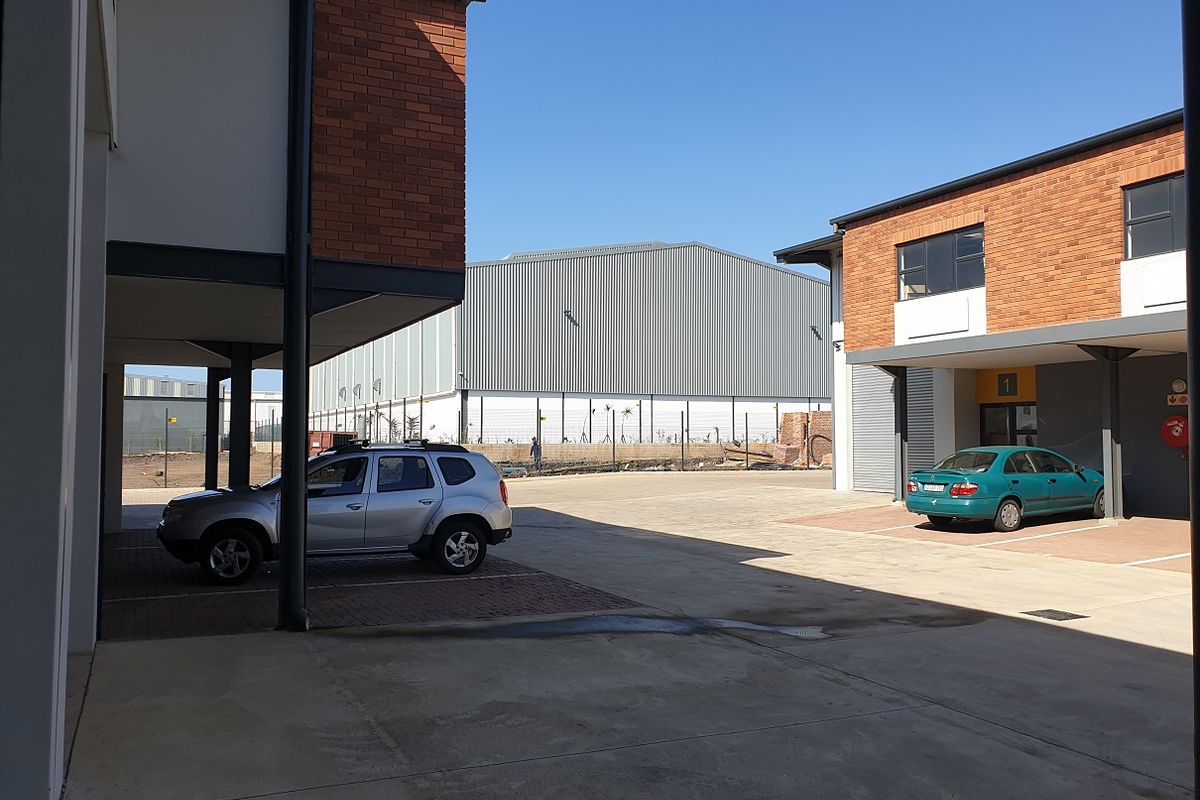 Exterior view of an industrial complex featuring brick facade buildings, covered parking bays, and a paved courtyard area.