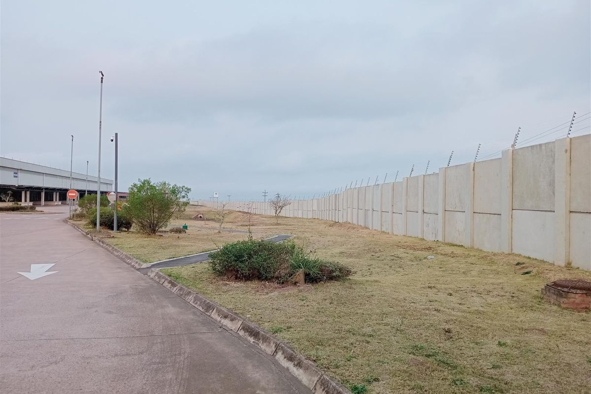 Exterior view of the industrial property grounds featuring a concrete perimeter wall with electric fencing and paved access road.