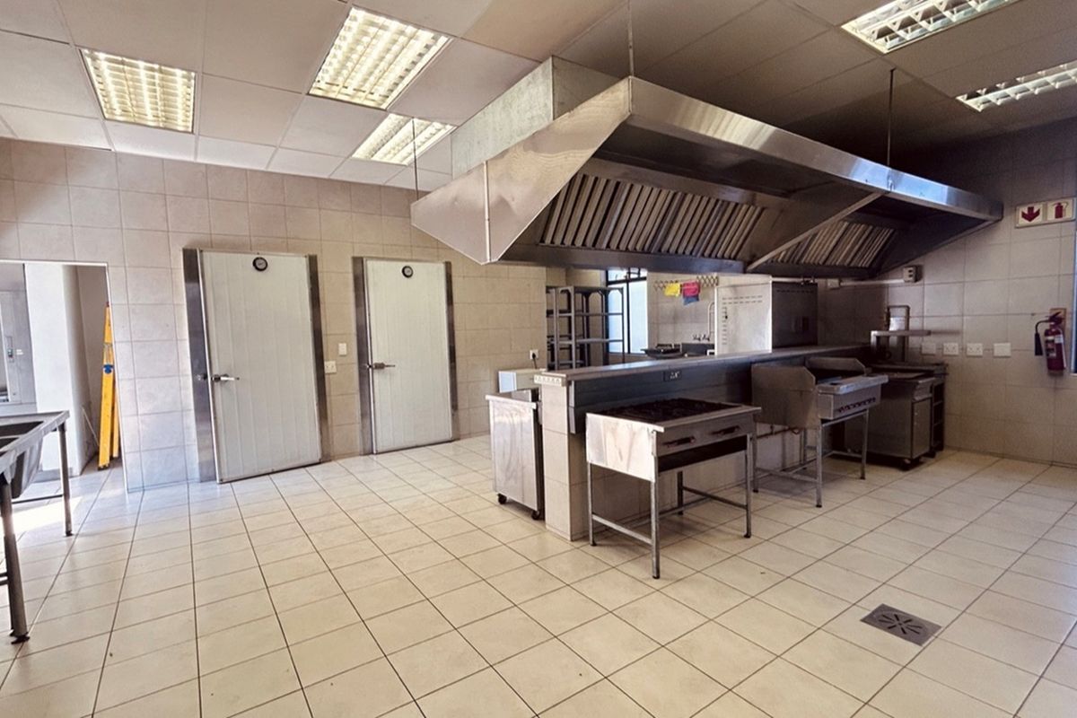 Commercial kitchen facility featuring stainless steel extraction canopy, tiled flooring, wall-mounted cold storage doors, and integrated stainless steel cooking stations.