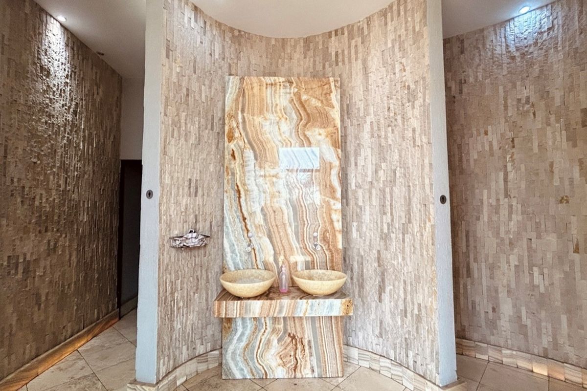 A modern bathroom vanity area featuring dual stone vessel sinks set into a striking onyx-style marble feature wall with textured stone cladding.