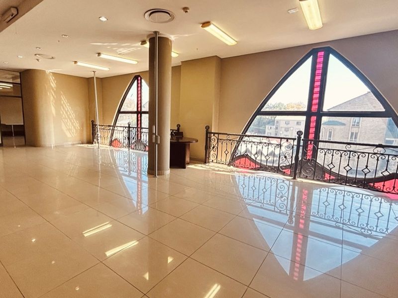 Spacious open-plan retail area featuring polished tile flooring, decorative wrought iron railings, and distinctive arched windows with red accent detailing.