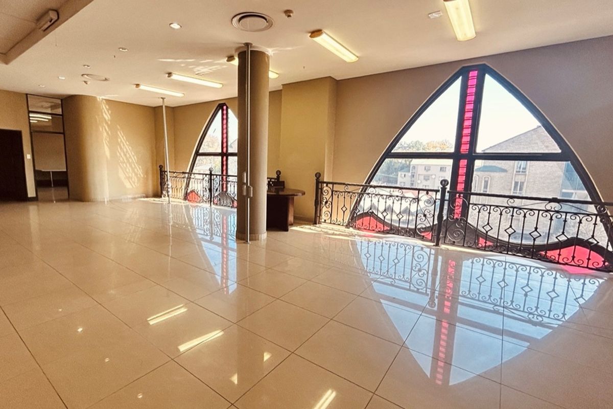 Spacious open-plan retail area featuring polished tile flooring, decorative wrought iron railings, and distinctive arched windows with red accent detailing.