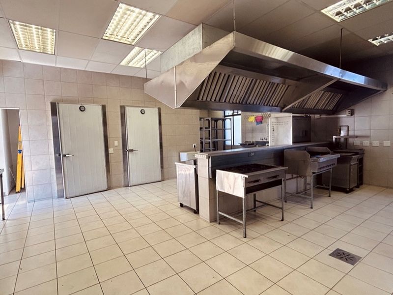 Commercial kitchen facility featuring stainless steel extraction canopy, tiled flooring, wall-mounted cold storage doors, and integrated stainless steel cooking stations.