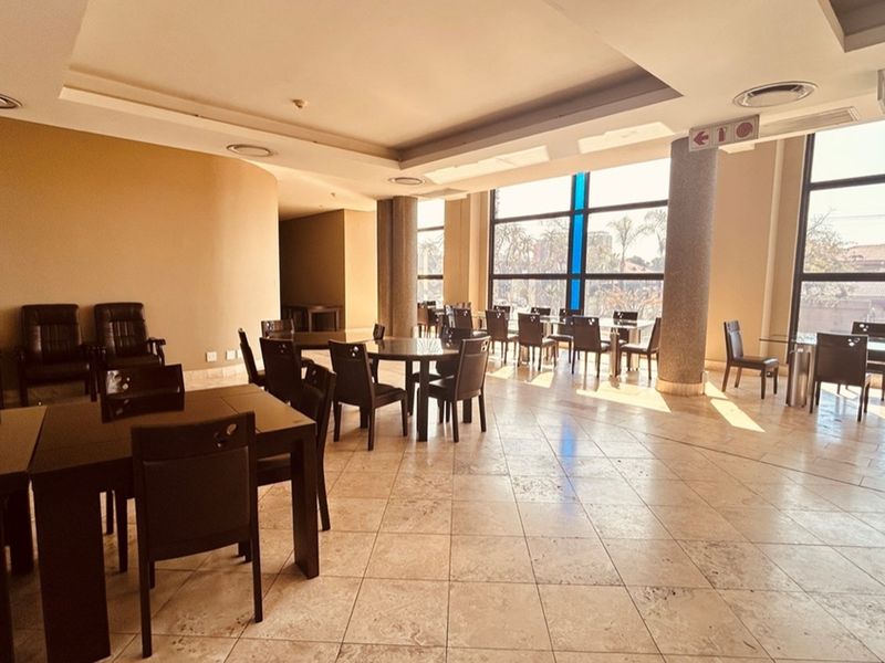 Spacious open-plan retail or dining area featuring large floor-to-ceiling windows, recessed ceiling lighting, and polished stone tile flooring.