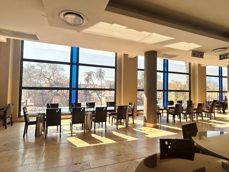 Spacious retail dining area featuring large floor-to-ceiling windows, tiled flooring, recessed ceiling lighting, and structural support columns.
