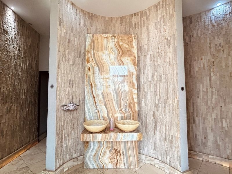 A modern bathroom vanity area featuring dual stone vessel sinks set into a striking onyx-style marble feature wall with textured stone cladding.