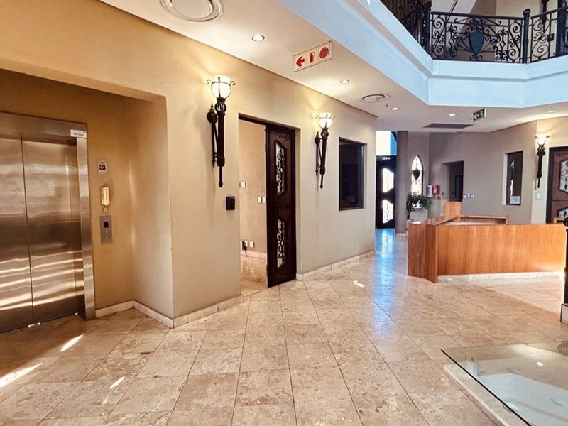 Spacious commercial lobby featuring polished stone flooring, a built-in reception desk, elevator access, and decorative wall sconces.