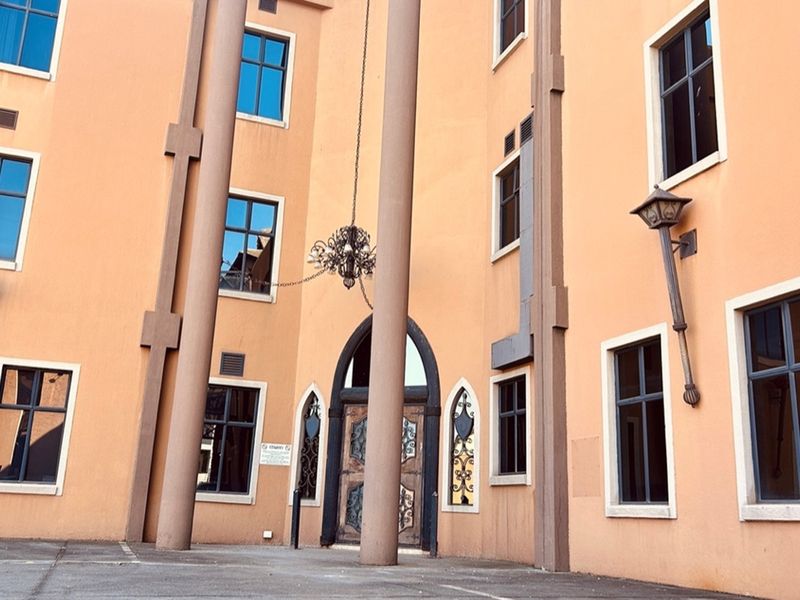 Exterior view of a retail building entrance featuring arched wooden doors, decorative columns, and wall-mounted lantern-style lighting fixtures.
