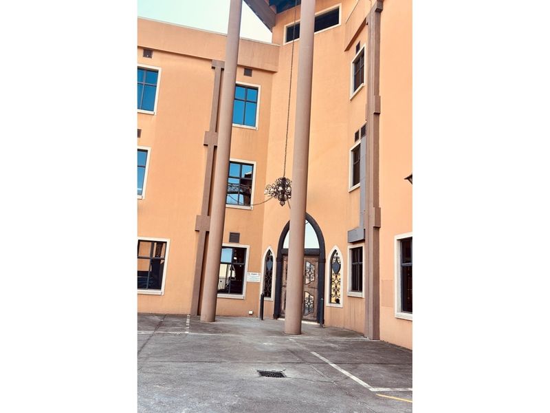 Exterior view of a multi-story retail building featuring prominent structural columns, arched entrance doors, and paved frontage.
