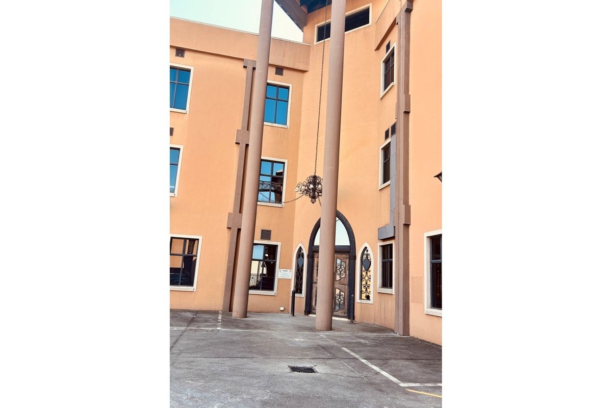 Exterior view of a multi-story retail building featuring prominent structural columns, arched entrance doors, and paved frontage.