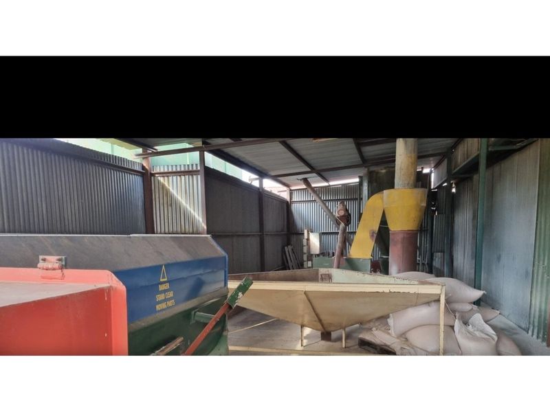 An industrial utility space on a farm featuring corrugated metal walls, concrete flooring, and fixed agricultural processing machinery.