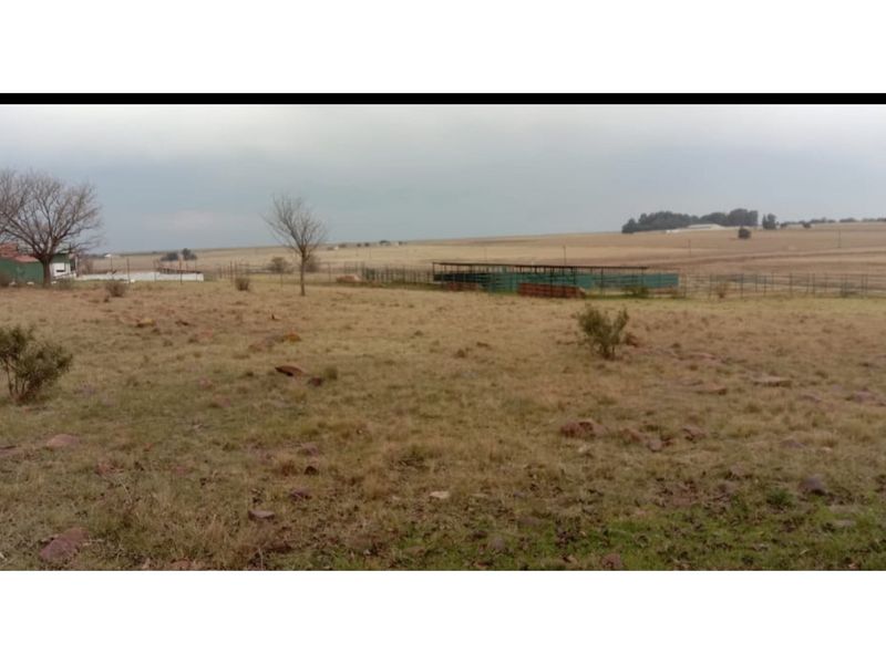 Expansive view of the farm landscape featuring open grazing land, wire fencing, and agricultural enclosures under an overcast sky.